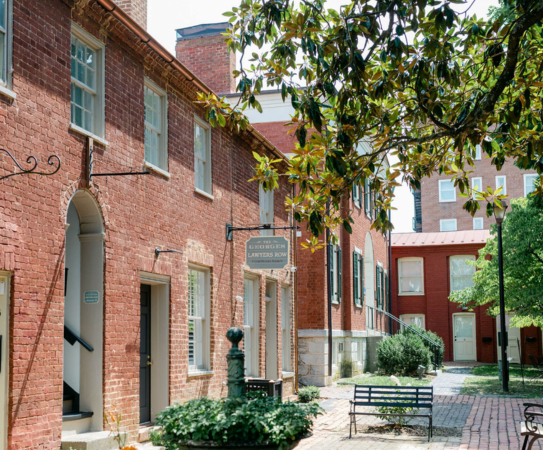TheGeorges_About_LawyersRow Exterior view of a two-story brick building on a brick courtyard. A sign reads The Georges Lawyers Row and there is a magnolia tree branch in the foreground.